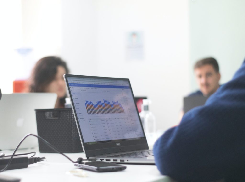 Colleagues sitting and talking at desks with a graph displayed on a laptop screen.